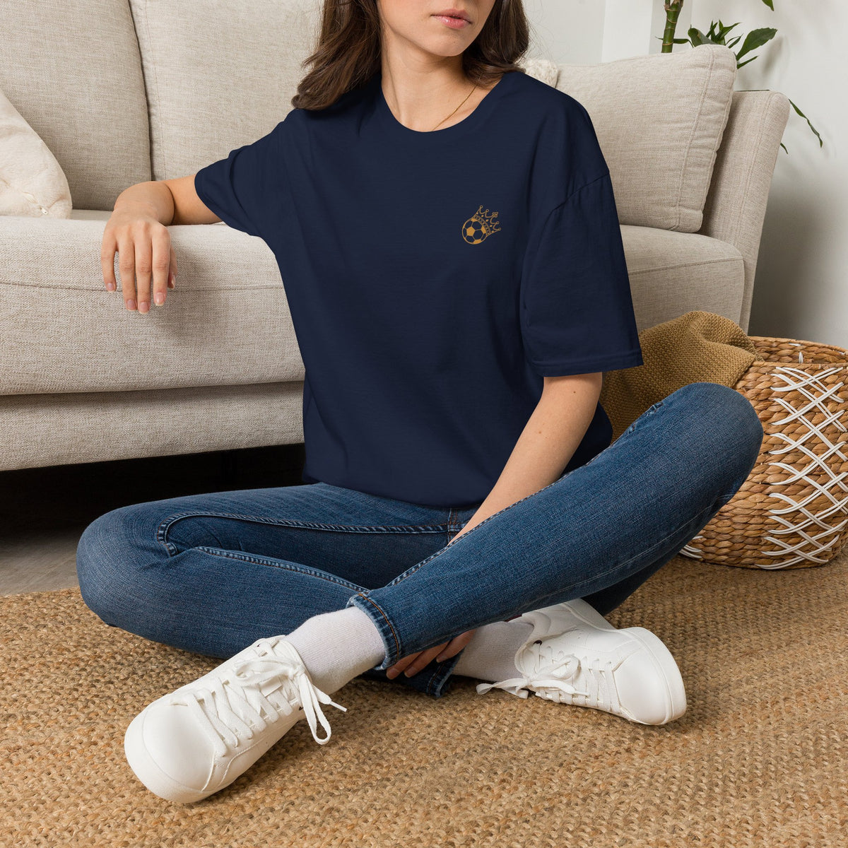 Cute Crowned Cat Pocket Tee — Minimal Embroidered Kitten T-Shirt modeled by a woman sitting on a floor, wearing jeans and sneakers.