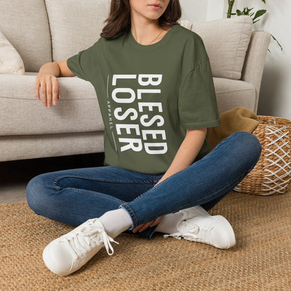 Person sitting on the floor wearing a Blessed Loser T-Shirt | Vertical Bold Text Graphic Tee in olive green.